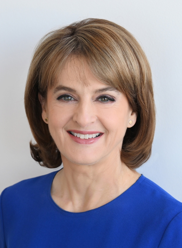 A headshot of Rebecca shows her to be a white woman in her 50s, with straight, bobbed brown hair and a fringe. She is smiling at the camera and wearing blue.