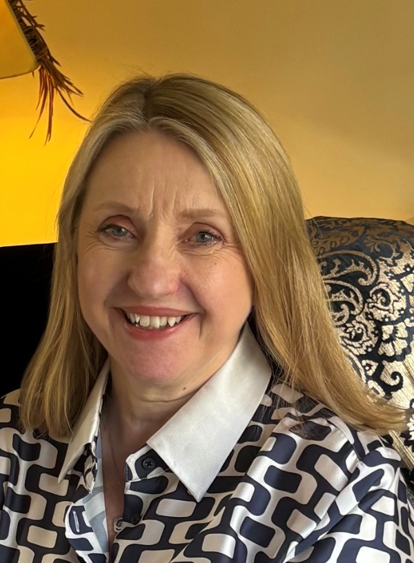 A headshot of Georgina Robbins shows her to be a white woman in her 50s with straight blonde, shoulder-length hair. She is smiling towards the camera and wearing a patterned black and shite shirt.