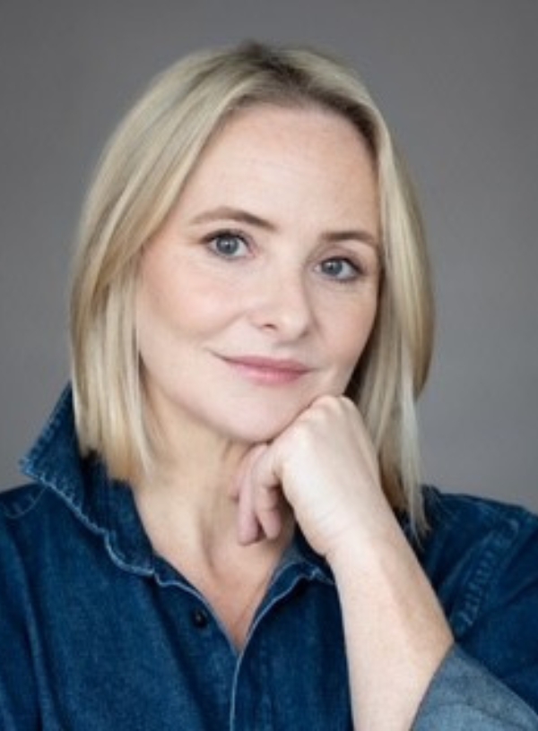 Photo is a headshot of Gemma Nixon. Gemma is a fair skinned woman in her 40s with straight, shoulder length blonde hair. She is wearing a dark blue denim shirt. Gemma is looking towards the camera, smiling, with her face resting on her fist.