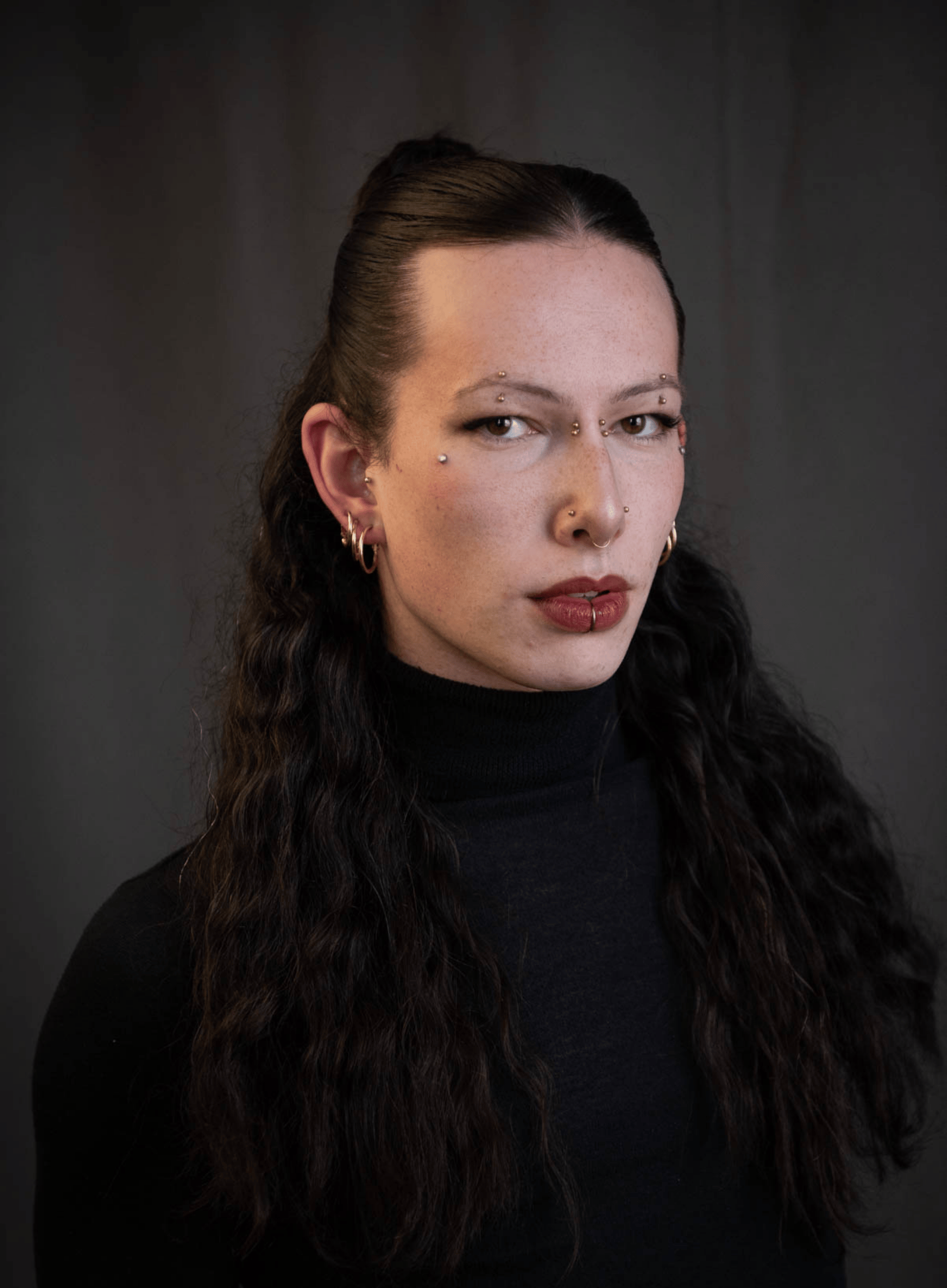Headshot of Jatie Tucker, a fair skinned woman with long dark hair tied back off the face, and multiple piercings.