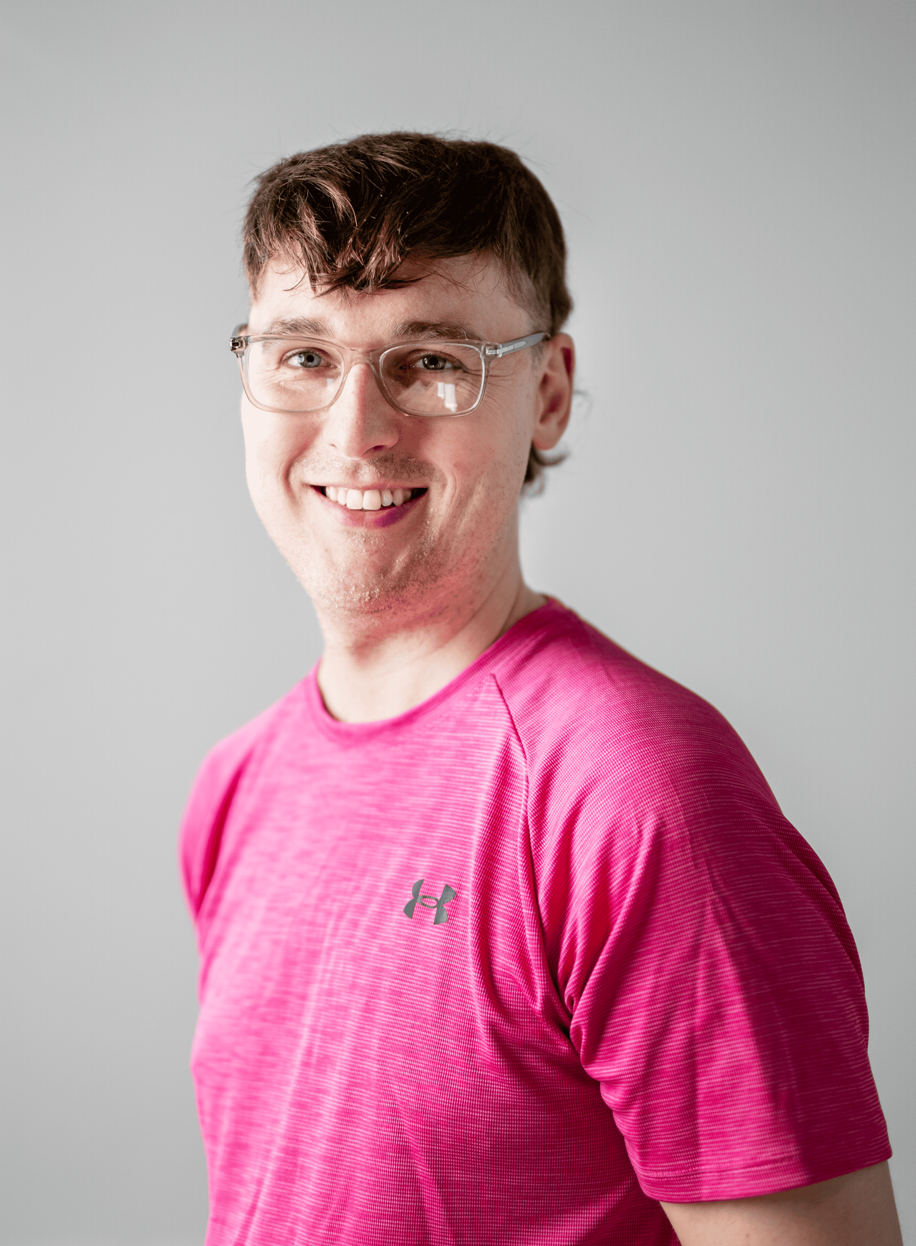 Headshot of Adam John Roberts, a fair skinned man with short brown hair, wearing transparent framed glasses and a pink t-shirt.